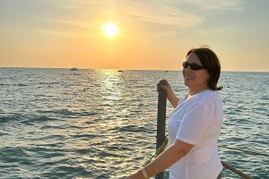 Was ist Lebensfreude_ Anita steht am Meer im warmen Abendlicht und schaut seitlich zurück; ein ruhiger Moment von Verbundenheit und innerer Klarheit.