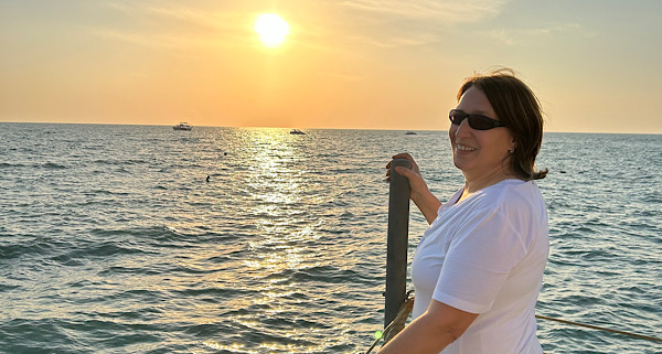 Anita steht am Meer im warmen Abendlicht und schaut seitlich zurück; ein ruhiger Moment von Verbundenheit und innerer Klarheit.