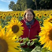 Anita Griebl steht in einem Feld voller Sonnenblumen und strahlt Ruhe, Präsenz und Lebensfreude aus.