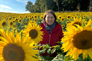 Anita Griebl steht in einem Feld voller Sonnenblumen und strahlt Ruhe, Präsenz und Lebensfreude aus.