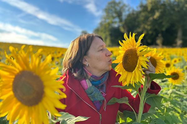 Anita lehnt sich liebevoll an eine Sonnenblume; ein Moment, der zeigt, wie Begleitung dir Zeit, Geld und Nerven sparen kann.