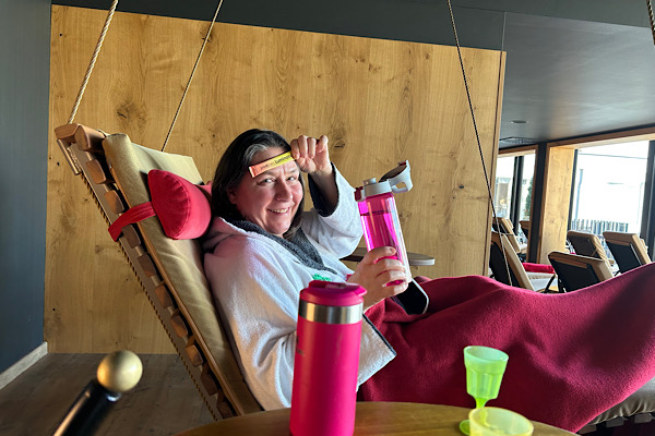 Heidi liegt in der Schaukelliege, hält das Powergetränk "Luminate" vor ihre Stirn und eine Wasserflasche in der anderen Hand.