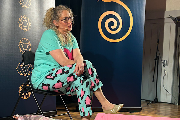 Michaela Hafner sitzt auf einem Hocker, hat die Beine übereinandergeschlagen, die Hände darüber verschränkt und wendet sich dem Publikum zu.