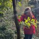 Anita Griebl steht im Wald, die Hand am Kinn, schaut nachdenklich in die Ferne, während ein Lichtstrahl ihr Gesicht berührt.
