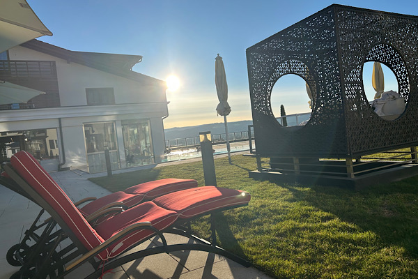 Außenbereich mit Sonnenliegen, einem Korbhaus zum Liegen und warmen Sonnenstrahlen im Hintergrund.