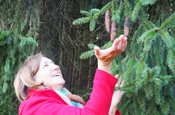 Anita Griebl berührt achtsam Fichtenzapfen im Wald – Symbol für den Prozess der Persönlichkeitsstärkung.