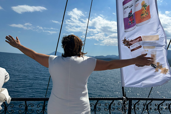 Ausblick – Anita Griebl im weißen Outfit mit offenen Armen an der Reling, Blick aufs Meer