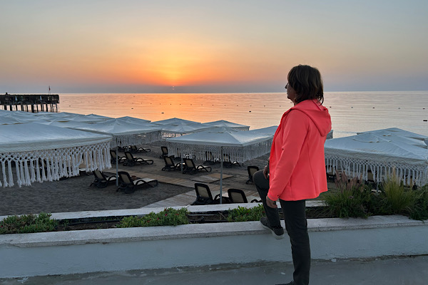 Anita Griebl steht seitlich am Strand im warmen Licht des Sonnenaufgangs und blickt ruhig in die Ferne – Symbol für Orientierung, Klarheit und inneren Weg.