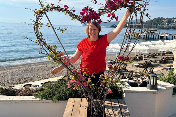 Erfolg durch Intuition – Anita Griebl mit geschlossenen Augen hinter einem Herz aus Bougainvillea am Meer.