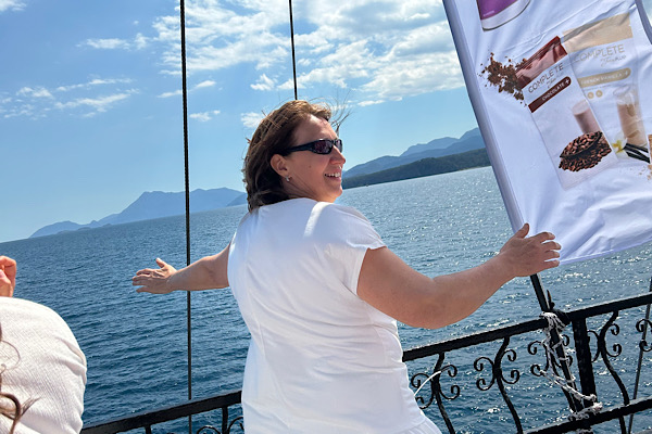 Phase 1 – Mut und Aufbruch: Anita Griebl am Schiff in weißer Kleidung vor dem Meer