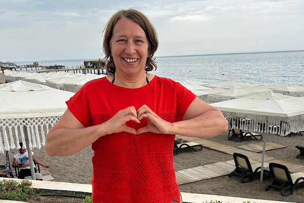 Frau steht am Meer und formt mit den Händen ein Herz vor dem Brustraum – Symbol für Herzöffnung, Verbindung und innere Klarheit.