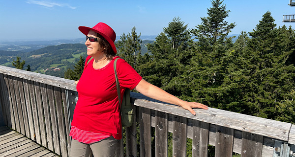 Anita Griebl steht auf einem Steg über den Baumwipfeln und blickt in die Ferne – Symbol für Klarheit und neue Perspektiven durch energetische Begleitung.