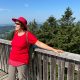 Anita Griebl steht auf einem Steg über den Baumwipfeln und blickt in die Ferne – Symbol für Klarheit und neue Perspektiven durch energetische Begleitung.