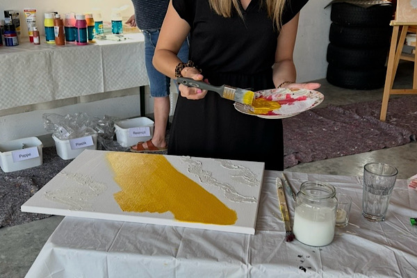 Eine Teilnehmerin taucht ihren Pinsel in goldene Acrylfarbe und malt intuitiv an ihrer Leinwand – nur Oberkörper und Hände sind sichtbar, in einer ruhigen und achtsamen Atmosphäre des Energie‑Mal‑Seminars.