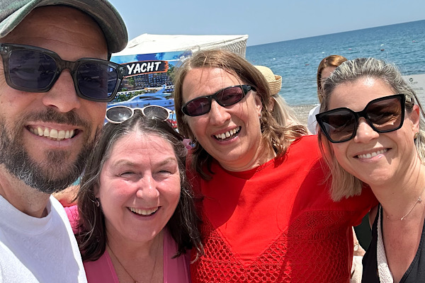 Heidi und ich stehen mit den Organisatoren Dennis und Claudia Gombkötö für ein Foto zusammen; im Hintergrund ist das Meer zu sehen.