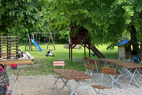 Biergarten der Waldschänke Grieshaus mit Tischen unter Bäumen und angrenzendem Kinderspielplatz.