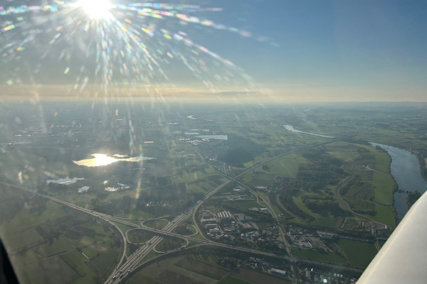 Blick aus einem Sportflugzeug auf die Landschaft rund um das Autobahnkreuz Deggendorf, durchzogen von einem einfallenden Lichtstrahl.