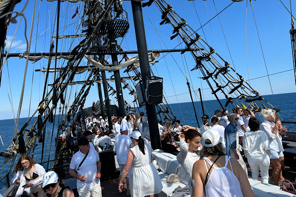 Teammitglieder in weißer Kleidung stehen auf dem Oberdeck eines schwarzen Piratenschiffs während der White‑Dresscode‑Bootsparty