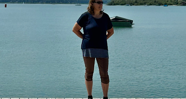 Anita steht auf einem Holzsteg am Ammersee und blickt seitlich über das Wasser; ruhige, natürliche Stimmung.