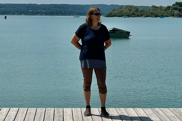 Anita steht auf einem Holzsteg am Ammersee und blickt seitlich über das Wasser; ruhige, natürliche Stimmung.