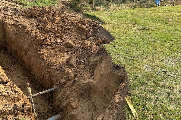 Tiefer Erdgraben im Garten mit sichtbarem Kabel – ein aufgeschichteter Boden, der alte Schichten freilegt.