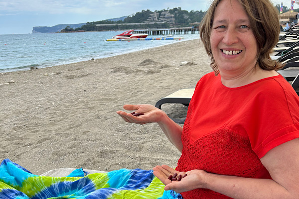 „Anita Griebl am Strand mit Vitalstoffen in den Händen – ein Moment von Pflanzenkraft, Licht und innerer Ruhe.