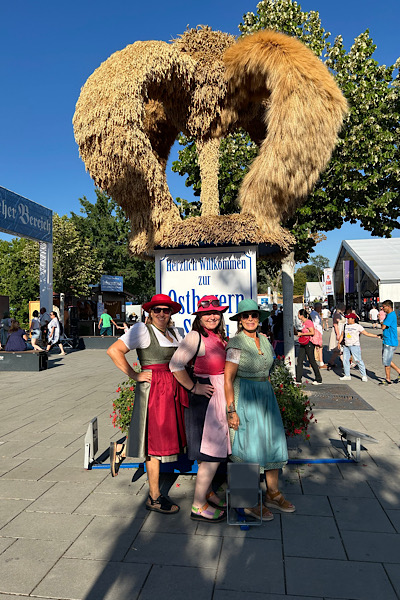 „Drei Frauen in Dirndl stehen vor der Erntekrone des Gäubodenvolksfestes.