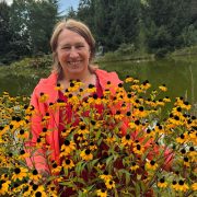 Anita Griebl inmitten gelber Blumen vor einem Weiher – ein naturverbundener Moment voller Lebensenergie.