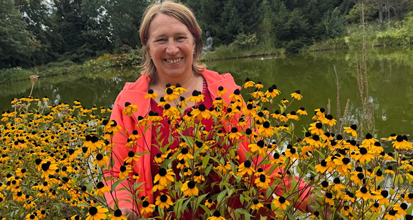 Anita Griebl inmitten gelber Blumen vor einem Weiher – ein naturverbundener Moment voller Lebensenergie.