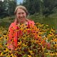 Anita Griebl inmitten gelber Blumen vor einem Weiher – ein naturverbundener Moment voller Lebensenergie.