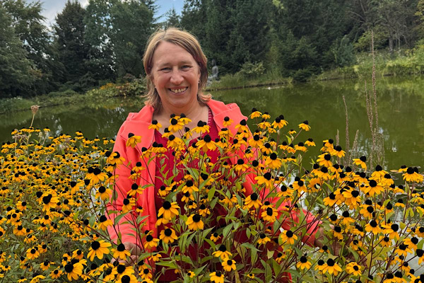 Anita Griebl inmitten gelber Blumen vor einem Weiher – ein naturverbundener Moment voller Lebensenergie.