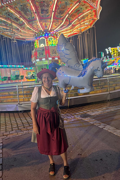 Anita steht vor dem Kettenkarussell und hält ein Luftballonpferd in den Händen.