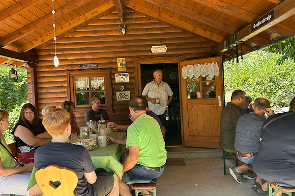 Mehrere Personen sitzen bei einer Grillfeier im Garten zusammen.