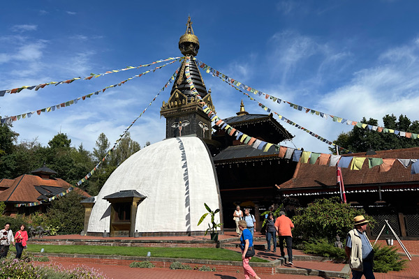 Nepal Himalaya Pavillon im Nepalpark, von außen fotografiert; bunte Gebetsfahnen hängen am Gebäude, im Hintergrund Garten und Bäume.