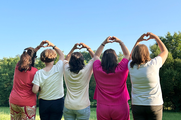 Fünf Frauen stehen von hinten sichtbar und formen mit ihren Händen Herzen über dem Kopf – ein Bild für Gemeinschaft, Dankbarkeit und berührende Verbundenheit.
