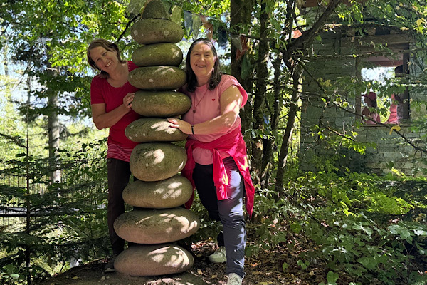 Zwei Frauen stehen seitlich an einer Steinsäule im Nepalpark, halten sich daran fest und lachen gemeinsam hervor.