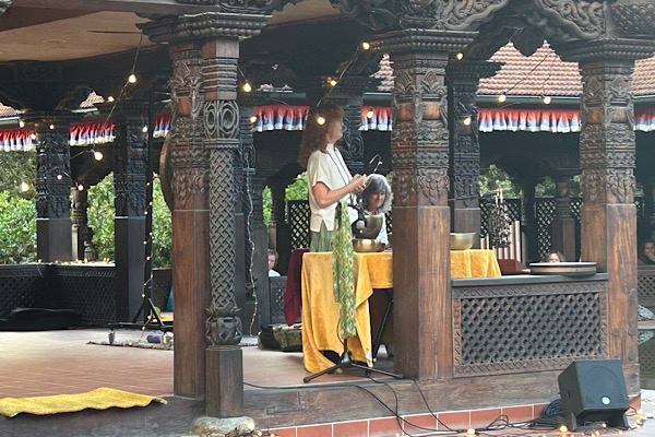 Izabela steht im Inneren des Nepaltempels und führt durch die Meditation. Die Klangschalen sind auf dem Tisch.
