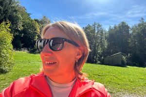 Monatsrückblick September 2026 2 Anita Griebl mit Sonnenbrille schaut seitlich aus dem Bild; hinter ihr liegen eine Wiese, ein Wald und Sonnenstrahlen im Hintergrund.