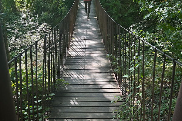 Hängebrücke von einem Ende zum anderen, mit den Beinen einer Person im Hintergrund – ein Bild für Unsicherheit, Druck und den Weg durch die Schwere.